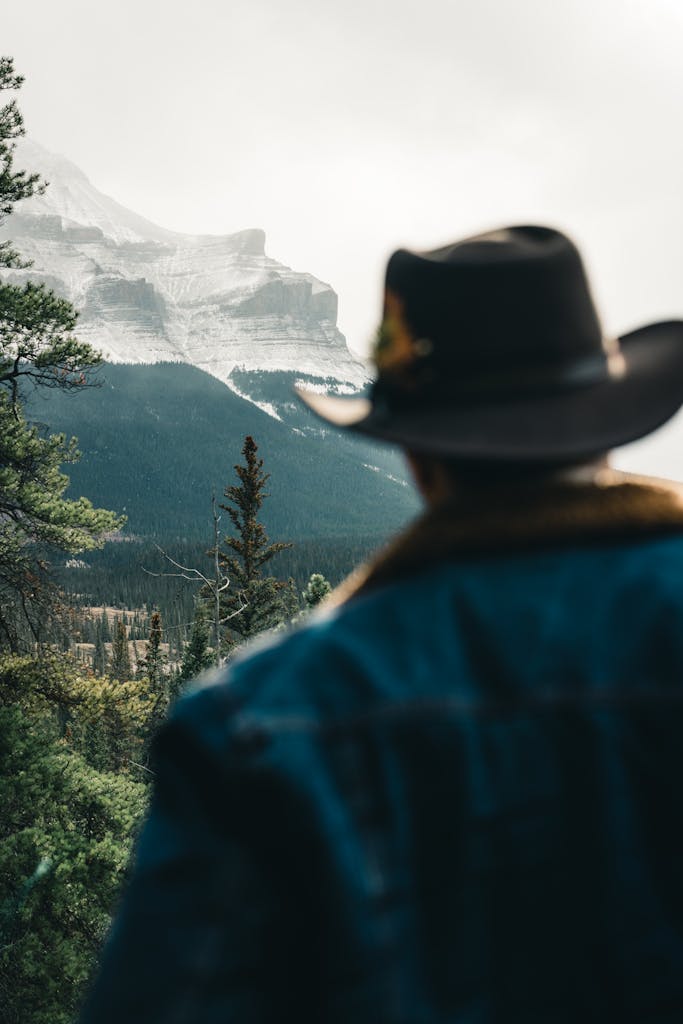 A cowboy in a denim jacket looks at the stunning mountains of Jasper, Alberta, Canada.